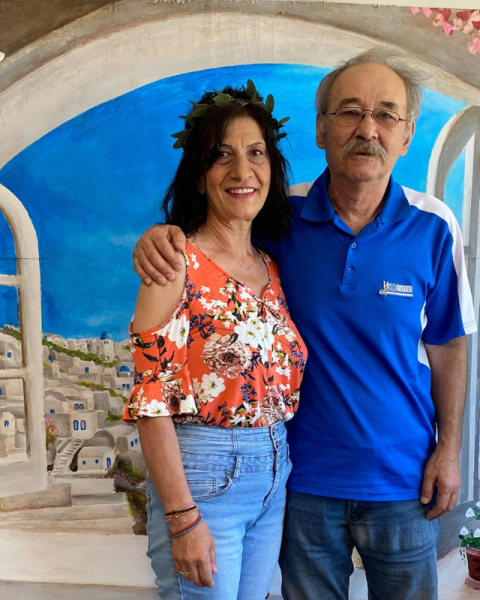 A man and woman smiling in front of a mural of santorini