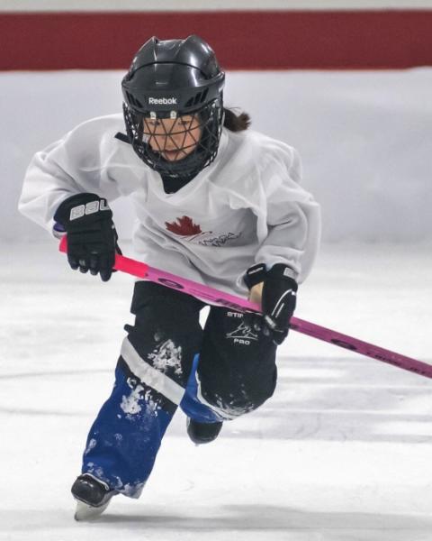 Young person skating with a ringette stick.