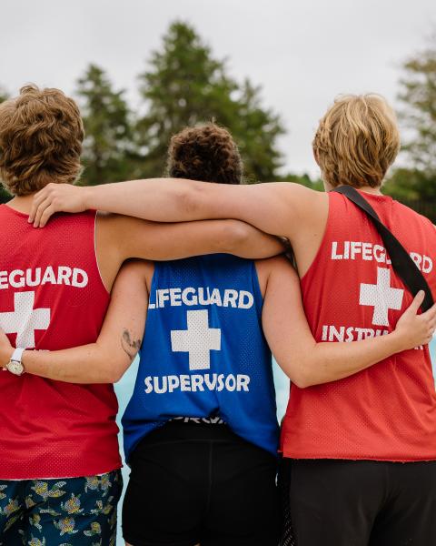Three lifeguards standing poolside, facing the swimming pool.