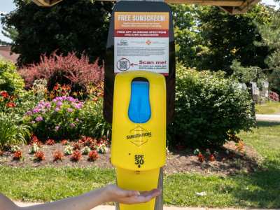yellow sunscreen dispenser attached to wood pole on riverfront trail