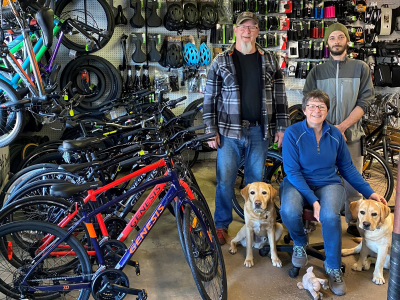 Bob's Sports Service team smiling in their shop with their two yellow labs