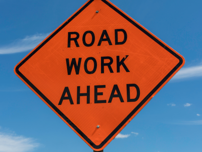 Orange diamond sign says road work ahead against blue sky