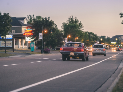rear view of a red vintage car driving down a street at dusk, business lights in the background