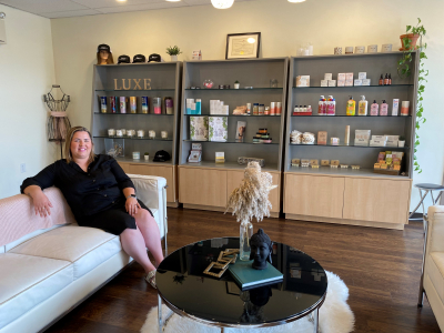 salon owner sits on white couch with products on shelf