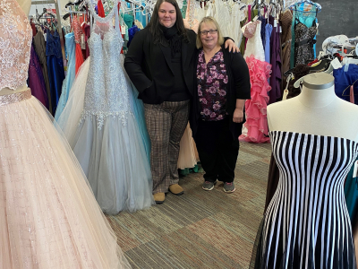 Business owners Annie and Joanne stand inside store surrounded by prom dresses