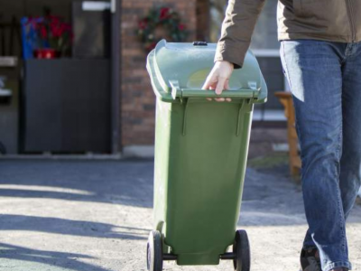 Man rolls green garbage bin to the curb